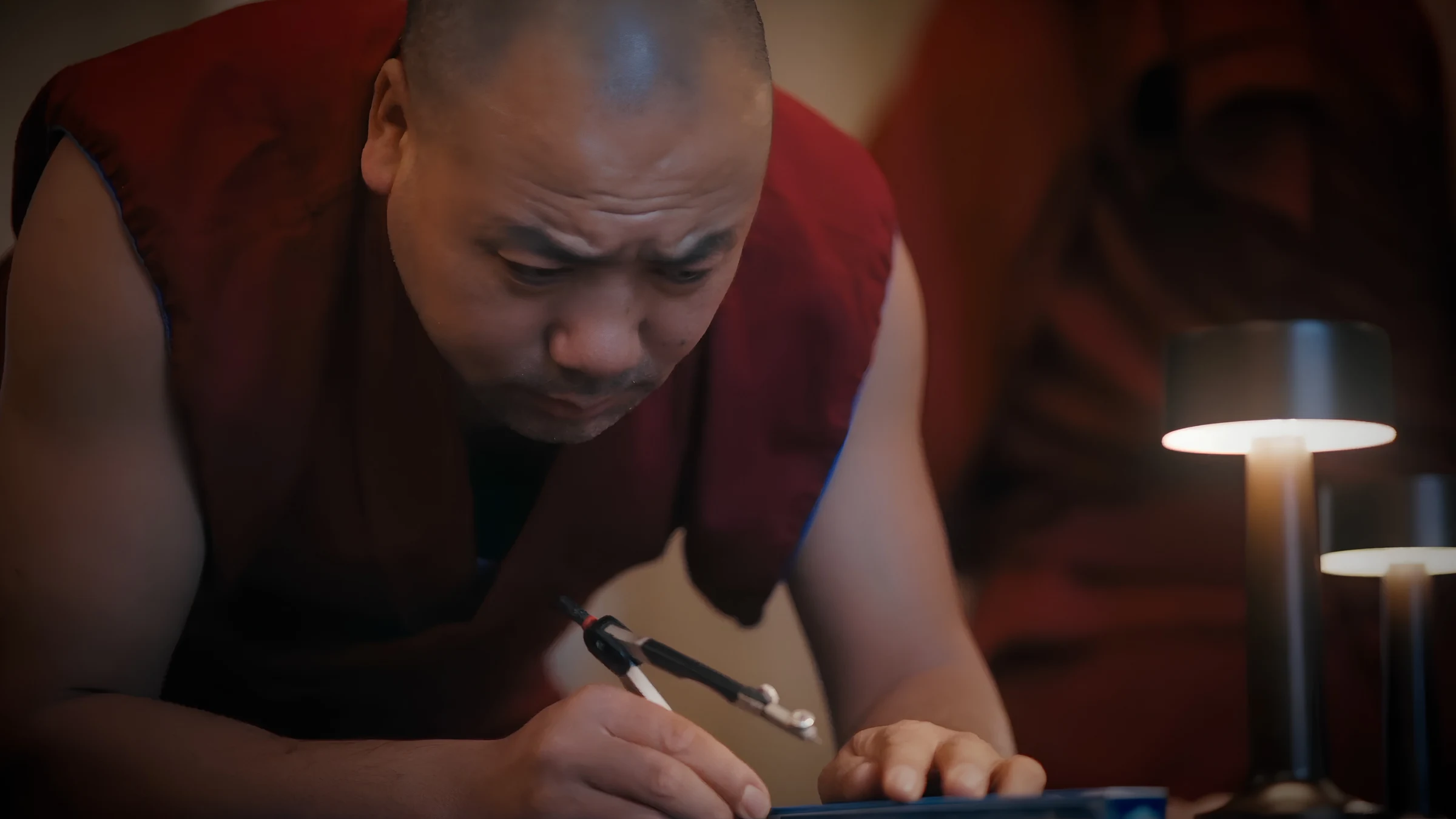 Senior monk carefully sketching out sand mandala pattern