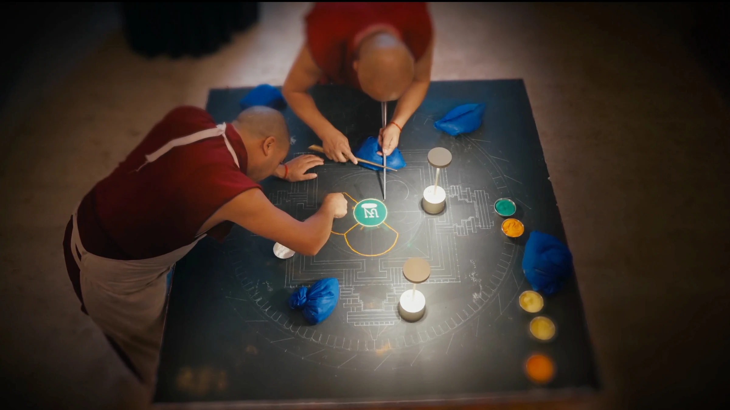 Senior monks placing grains of sand to form mandala pattern