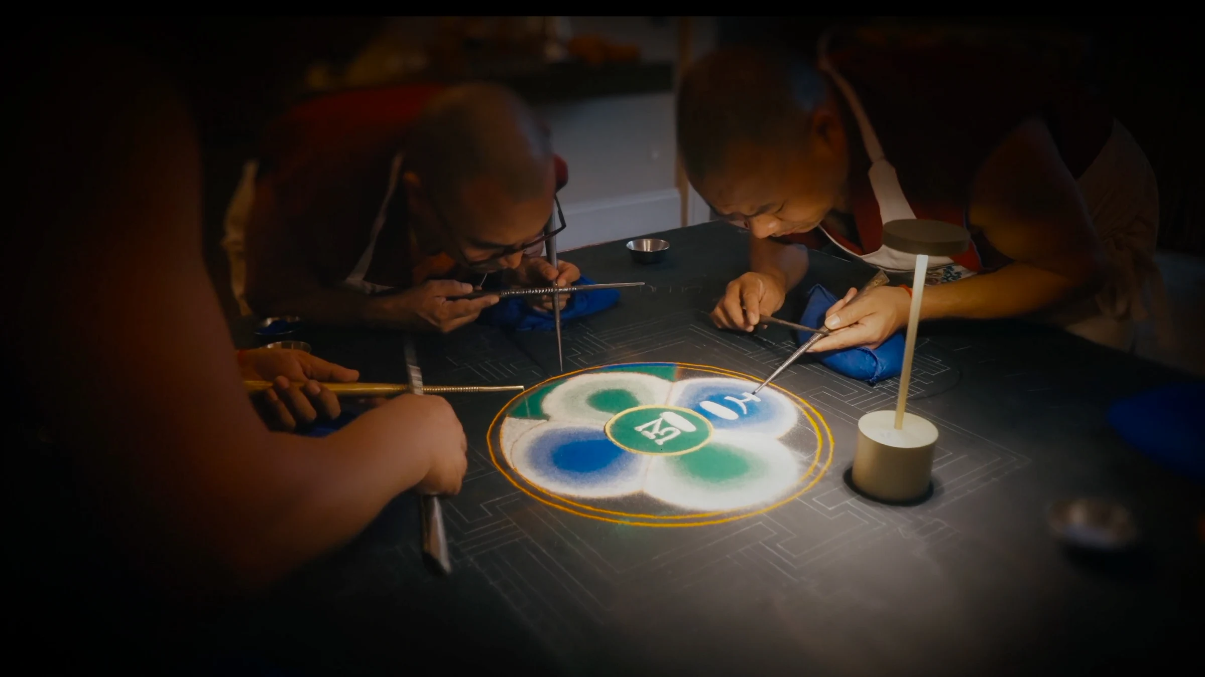 Senior monks meticulously placing grains of sand into their design
