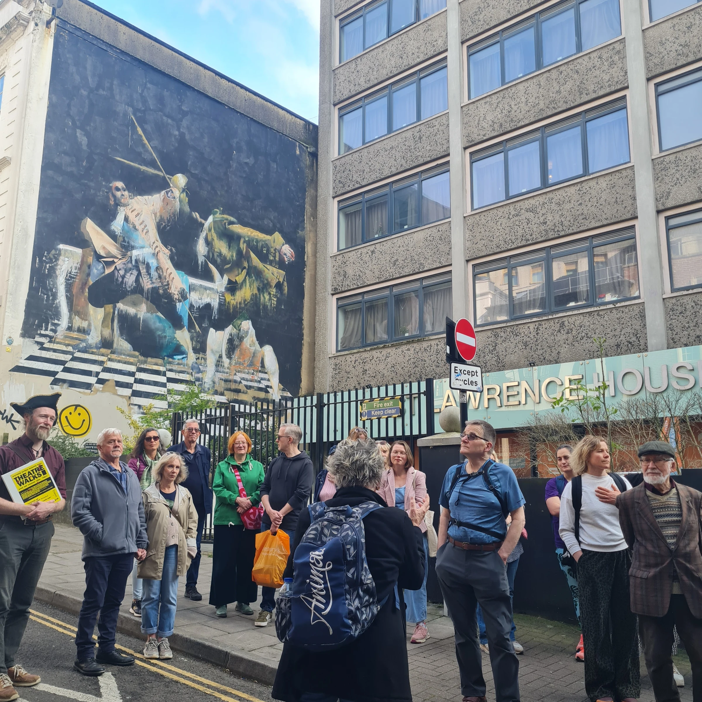 A group stops at the old city walls, below a huge piece of street art, at the Bristol Walk Fest launch night walk