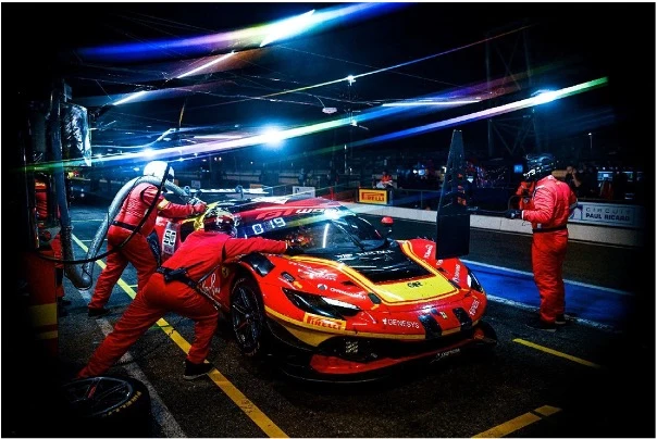 A Ferrari GT race car undergoing a precise nighttime pit stop, capturing the high-performance environment of Ferrari Competizioni GT.