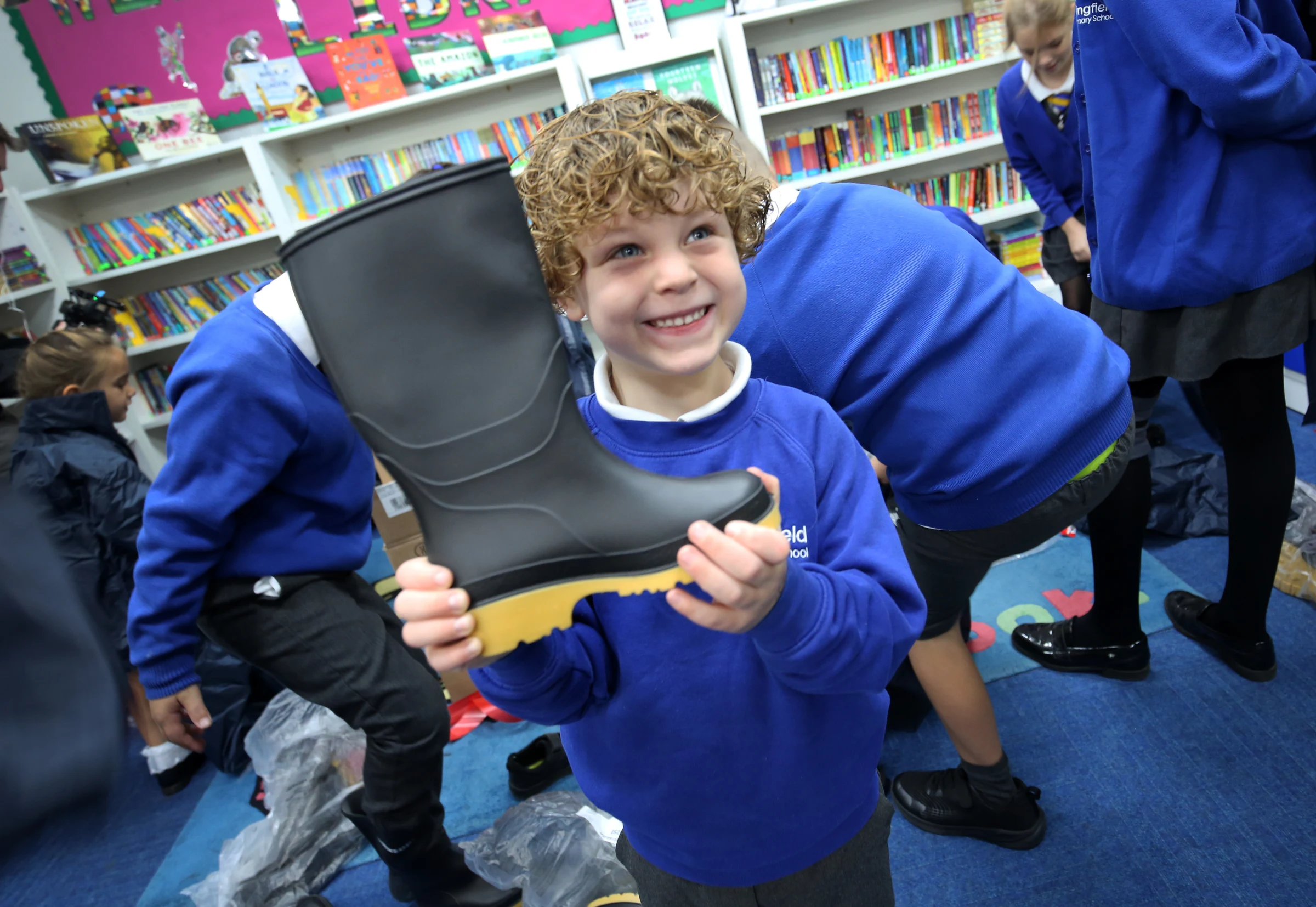 Young state priamry school pupil gleefully grabs his Wellie Boot. Gemma Hunt and children mark the latest Waterproofs & Wellies delivery.